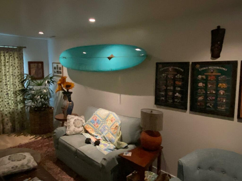 Angled Up Acrylic Surfboard Rack holding a teal colored longboard in a living room setting.