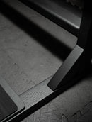 Lower portion of the flat black surf board freestnading rack shown in flat black. The red-oak made rack shows the grains of wood through the black coloring.