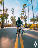 Shortboard bike rack shown in action on the middle of the street while a girl rides the bike. There are palm trees in the background.