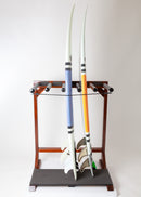 Finished foamy surfboard rack shown straight ahead holding 2 performance shortboards one with blue stripes, the other with orange stripes. The wooden rack is made of a dark colored mahogany that has high gloss. The boards are sitting on the black foam pad at the bottom of the storage rack.
