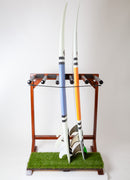 Front main picture of finished grassy surf rack that can hold up to 5 surfboards. The rack is made of a dark colored wood with a faux grass base, and is shown holding two surfboards.