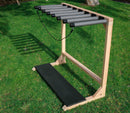 Foamy freestanding surfboard mount shown in a sanded wood finish. The rack is shown on a lawn that is vibrant green in color. There is a tree in the background.