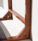 Close-up detail shot of the lower half of the finished foamy surf rack, showing the color of the dark wood, and the high-gloss finish. The rack is sitting on a cream colored carpet, with an off white wall next to it.