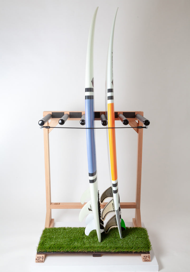 Grassy surfboard rack that can hold up to 5 surfboards. The wooden rack is shown holding two surfboards one blue, and one orange, while they sit on the rack's faux grass base. 