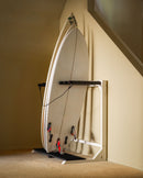 White vertical freestanding rack shown holding multiple surfboards next to a staircase. The rack is in a living room, and has beige walls and carpet.