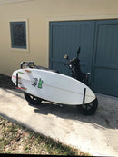 Moped rack parked out front of a garage with a lost surfboards fishy shape board in the rack.