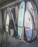 Several epic surf racks freestanding racks holding many surfboards at the Scripps Institute for Oceanography. There are a variety of surfboards in the rack from longboards to shortboards.