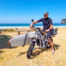 man in wetsuit on white e-bike using longboard rack at the beach to go surfing