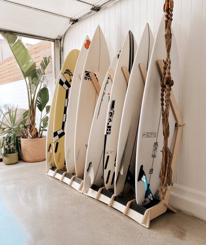 Wood Freestanding Surfboard rack displayed inside a high end garage with marble floors.  there are several plants to the side of the surfboard racks.   There are numerous surfboards organized in the racks. 