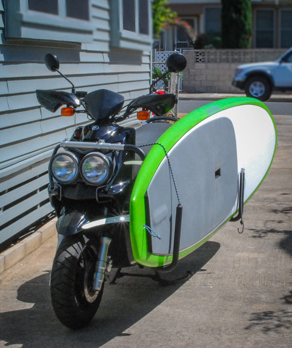 Front view of the SUP Moped rack - For Stand Up Paddle Boards & Surfboards. The moped is parked in a driveway, and there are houses in the background. 