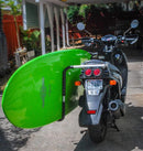 Moped shown holding a green Stand Up Paddleboard. The bike is parked in a driveway under a car port.