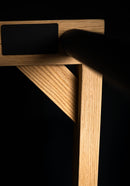 Grassy Freestanding surf rack detail shot of upper right corner focusing on the high quality red oak wood grain. Has dramatic lighting with a black backdrop. lots of shadow and mood showing the strength of this storage rack.