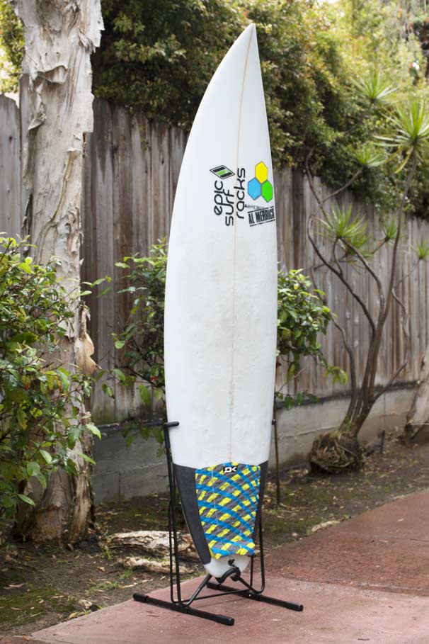 The Steel Single Rack shown on the side of a yard with bushes in the background.  The metal freestanding surfboard rack is holding a channel islands surfboard in the vertical position.  The rack is entirely freestanding.  