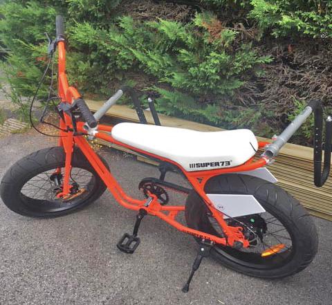 Super 73 orange and white e-bike with the longboard rack mounted to the front and rear of the bike. 