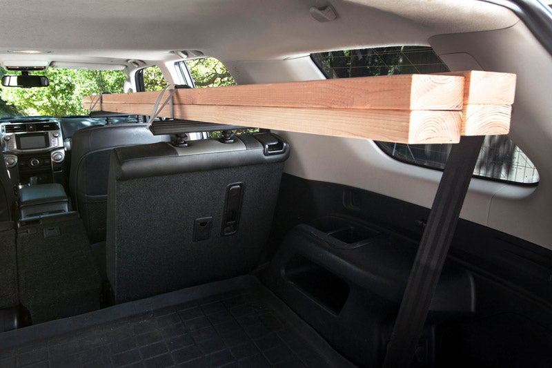 Headrest rack being used inside a car used to transport lumber.  There are 4 2x3" boards being transported securely on the head rest rack.  