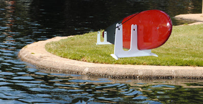 SUP & Surfboard Touring Rack for Docks and Piers shown on a plot of grass next to a lake. The white SUP rack is holding a single red stand up paddle board rack.