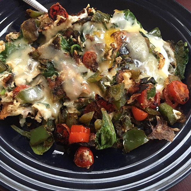 Picture of a dark blue plate with some eggs and vegetables.  There looks to be melted cheese on top of the eggs with a variety of spices.