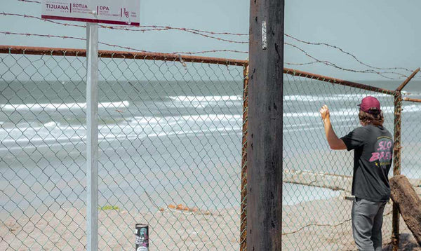 Surfer behind a barbed wire fence checking the waves at a beach break.