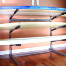 3 Level SUP rack shown holding several watercraft in a room with a peach colored call.  The rack is completely freestanding.