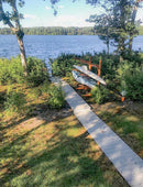 3 level log kayak rack in canyon brown shown next to some bushes by the side of a pond.  There is a wooden walkway leading to the pond, going right past the log kayak and SUP rack. 
