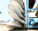 5 level SUP rack outdoors holding several watercraft and a small kayak on the bottom.  The rack is next to a wooden structure holding other watercraft. 