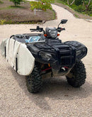 Black all terrain vehicle 4x4 (ATV) on a gravel road. The bike has a surfboard rack attached to the side of it, with the board in a protective board bag. 