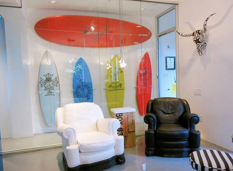 Board room shown with several surfboards mounted vertically behind a glass wall.  There is a white and a black chair in the foreground.
