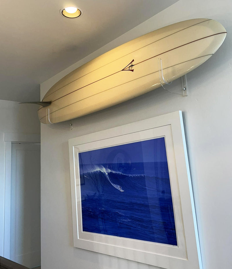 acrylic surfboard wall rack being held in a hallway above a photo of a hawaiian wave