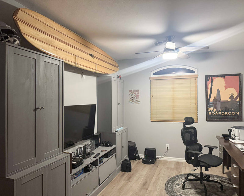 Clear acrylic longboard wall rack shown storing a balsa longboard above some cabinets in a home office. 