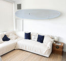 Acrylic wall rack shown holding a blue longboard in someone's living room, above a couch.  The rack is completely clear showing the board "hovering" off the wall. 