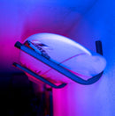 Angle 45 metal wall rack shown holding a single surfboard.  Purple and blue lights are shown lighting up the walls. 