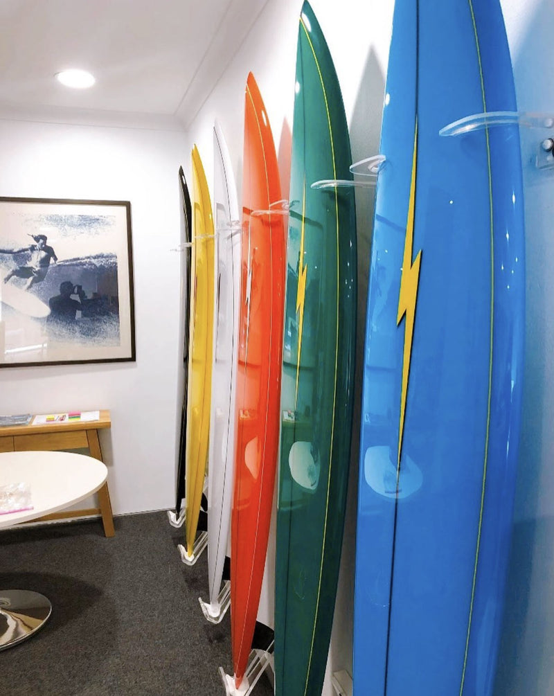 Side picture of several surfboards being mounted next to one another using the acrylic surfboard vertical wall racks. The surfboards are various colors from blue, green, red, white, yellow, and black.