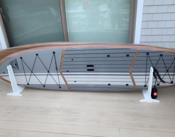 White dock rack shown holding two stand up paddle boards on a customer's porch.  The rack is white and the boards are a grey and brown.  The rack is setup right next to the house.