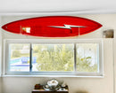 Red (signed) Gerry Lopez surfboard with a lightning bolt design mounted on a wall using the acrylic wall surfboard hangers above a window.