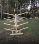 Side profile of the 8 boat freestanding log Kayak and SUP/Canoe rack. Shown on the grass holding one Blue Stand Up Paddleboard, with Trees and lawn furniture in the background.