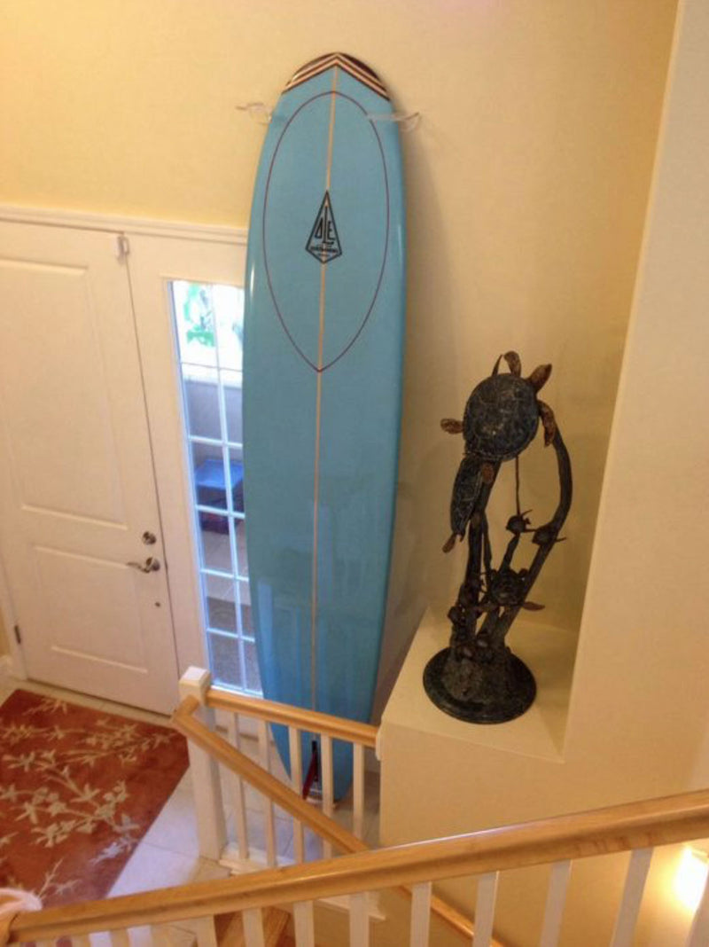 Customer photo of the acrylic vertical wall rack holding a baby blue longboard at the bottom of a staircase.  