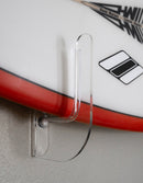 Clear plastic hook attached to a red and white surfboard with a logo on a gray surface.
