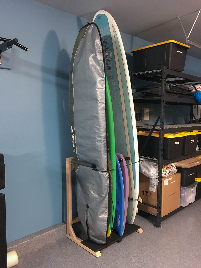 Customer photo of a standing surfboard rack holding several boards.  The storage rack is holding both longboards and shorboards.  There is a blue wall in the background, and there is a storage rack next to the surfboard rack. 