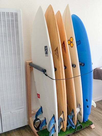 Customer photo of the grassy freestanding surfboard rack shown holding 5 shortboards.  The rack is sitting on a wooden floor. 