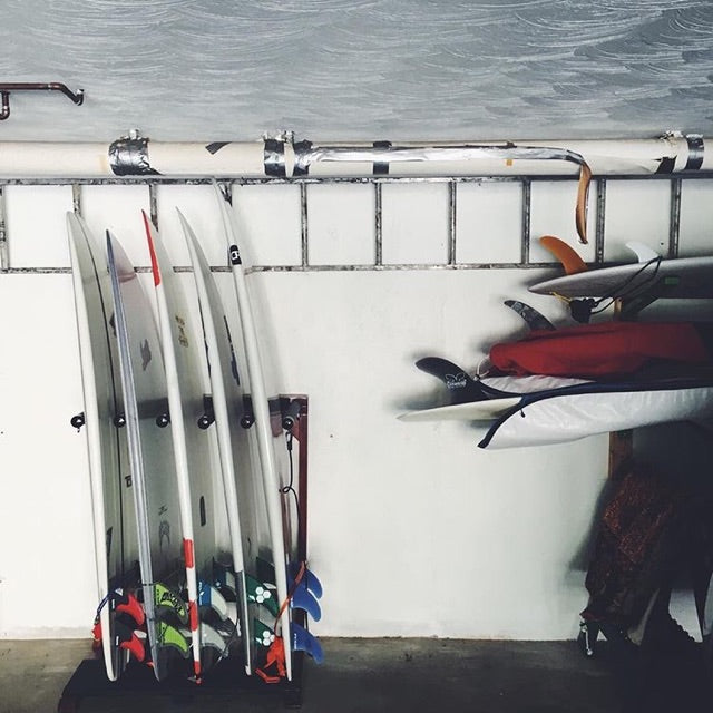 Finished Foamy surf rack shown in a garage holding 5 white shortboards, in an upright vertical position. There are several other surfboards in board bags to the right of the rack.  
