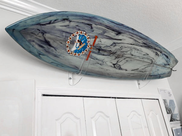 Blue surfboard with black swirls being held over a closet using clear acrylic wall mounts.