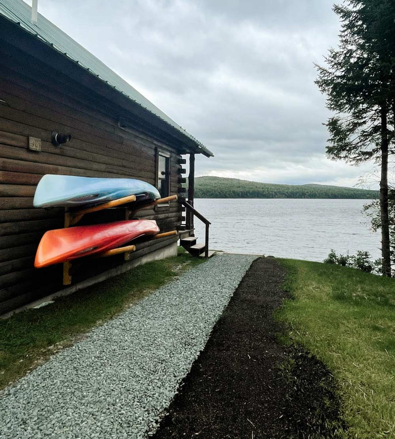 Two Kayaks mounted on the side of a log cabin and a granite pathway leading to a lake.