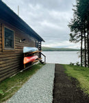 log cabin on a lake with two kayaks mounted to the side of the house with a log kayak rack. 