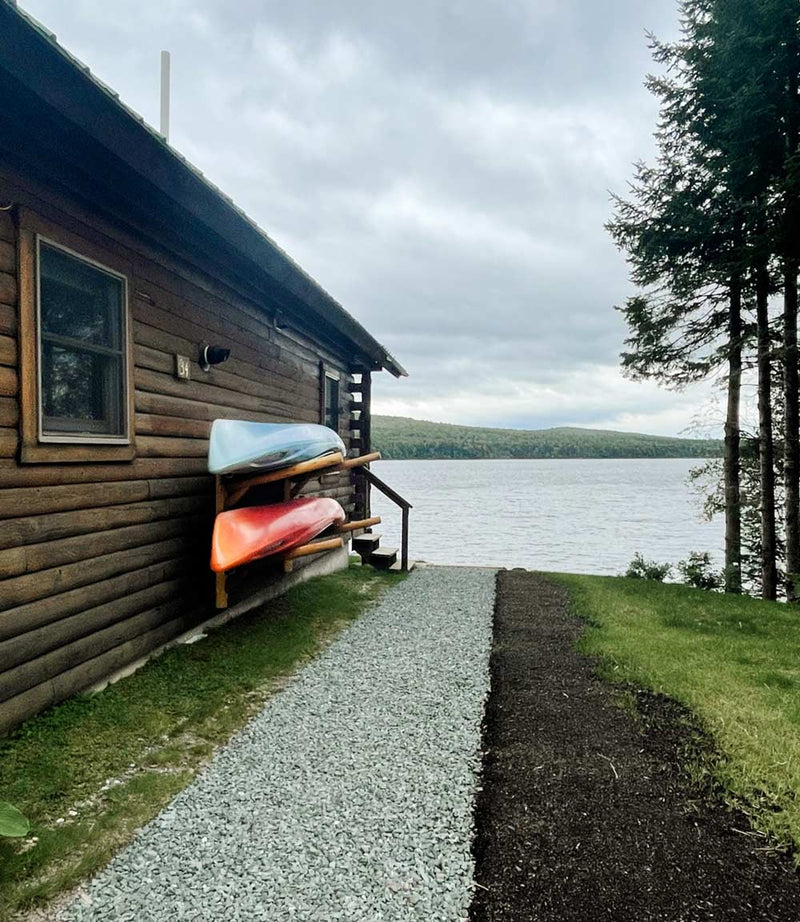 log cabin on a lake with two kayaks mounted to the side of the house with a log kayak rack. 