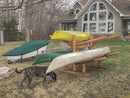 Free Standing Log kayak rack holding several canoes in the backyard of a beautiful home.  There appears to be a cute dog sniffing around the kayak rack. 
