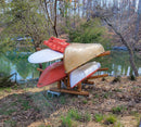 Kayak Log rack holding multiple watercraft next to a pond.  The rack is holding a Stand Up Paddle Board, a Canoe, and two Kayaks. 