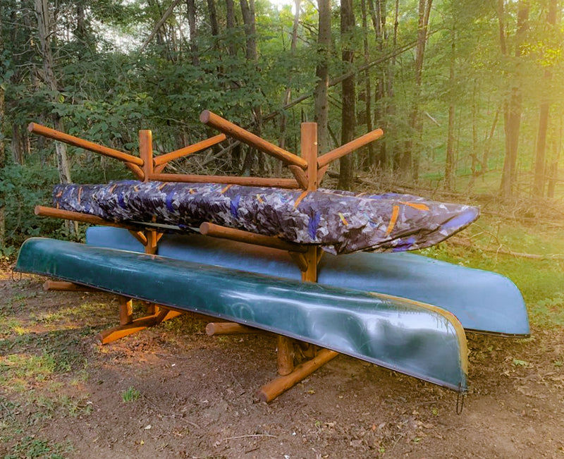 Log Kayak rack in canyon brown wood finish that is holding several watercraft.  There are two large Canoes on the bottom levels, with two kayaks being held in the middle level.  The top levels of the Kayak / Canoe Rack are empty. 