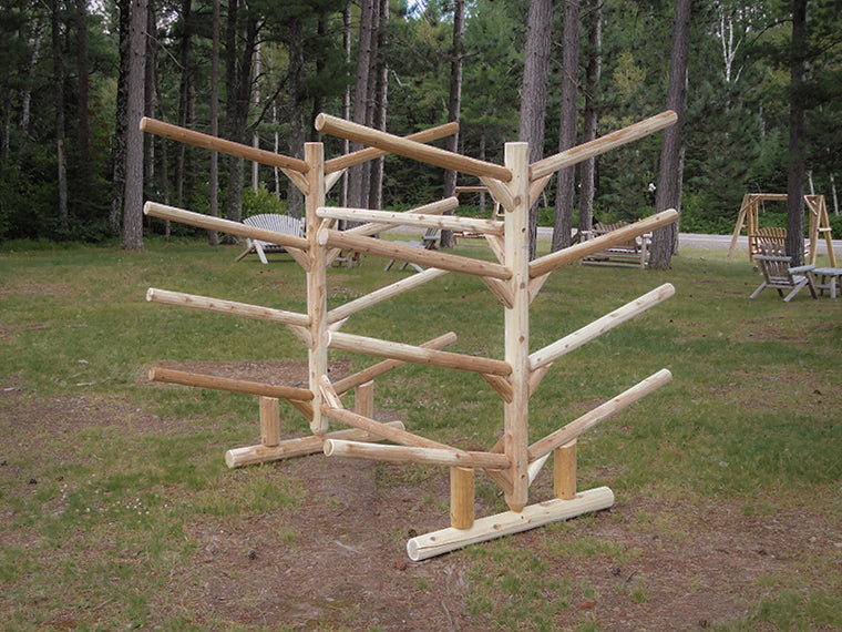 8 Slot watercraft freestanding storage rack made of wooden logs with no boats in it. Sitting on grass in the woods with some chairs in the background.