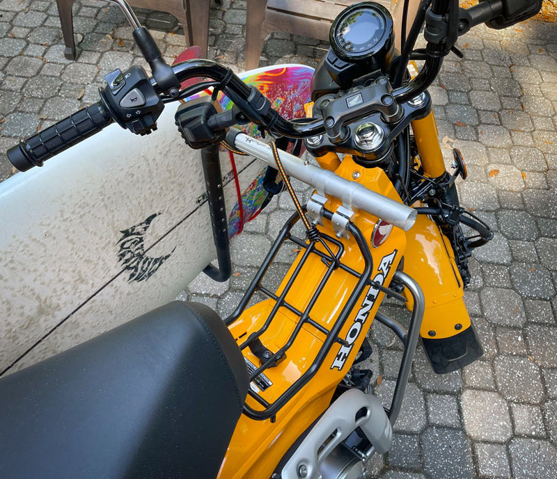 Close up view of a honda moped with a surfboard rack attached. The picture shows the front mount point of the surf rack attached to the mopeds luggage rack.