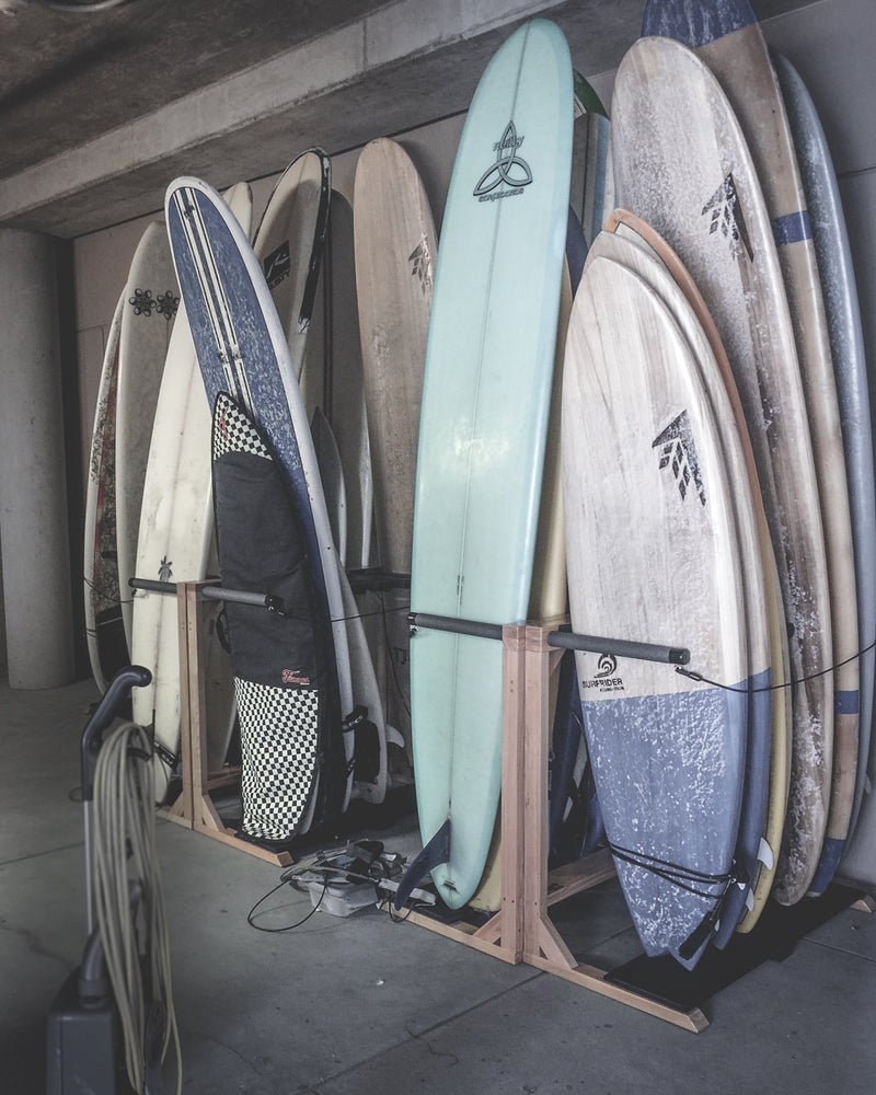 Several epic surf racks freestanding racks holding many surfboards at the Scripps Institute for Oceanography.  There are a variety of surfboards in the rack from longboards to shortboards. 